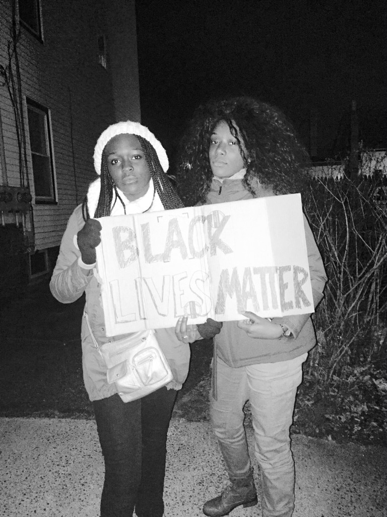 Here, young Efe Airewele on the left, a student of Phillips Academy, Exeter in New Hampshire and her friend, Holly Mondsier, a student of Kipp Academy Lynn Collegiate High School in Lynn, Massachusetts answered the call of civil liberties and human rights by participating in the protest. Their placard reads: “Black Lives Matter.”